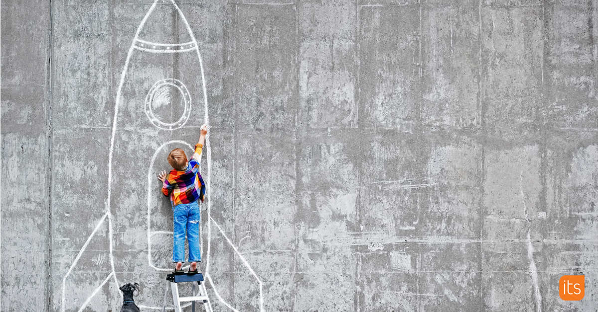 Foto av en elev som står framför en betongvägg med en krita i handen och ritar en raket.