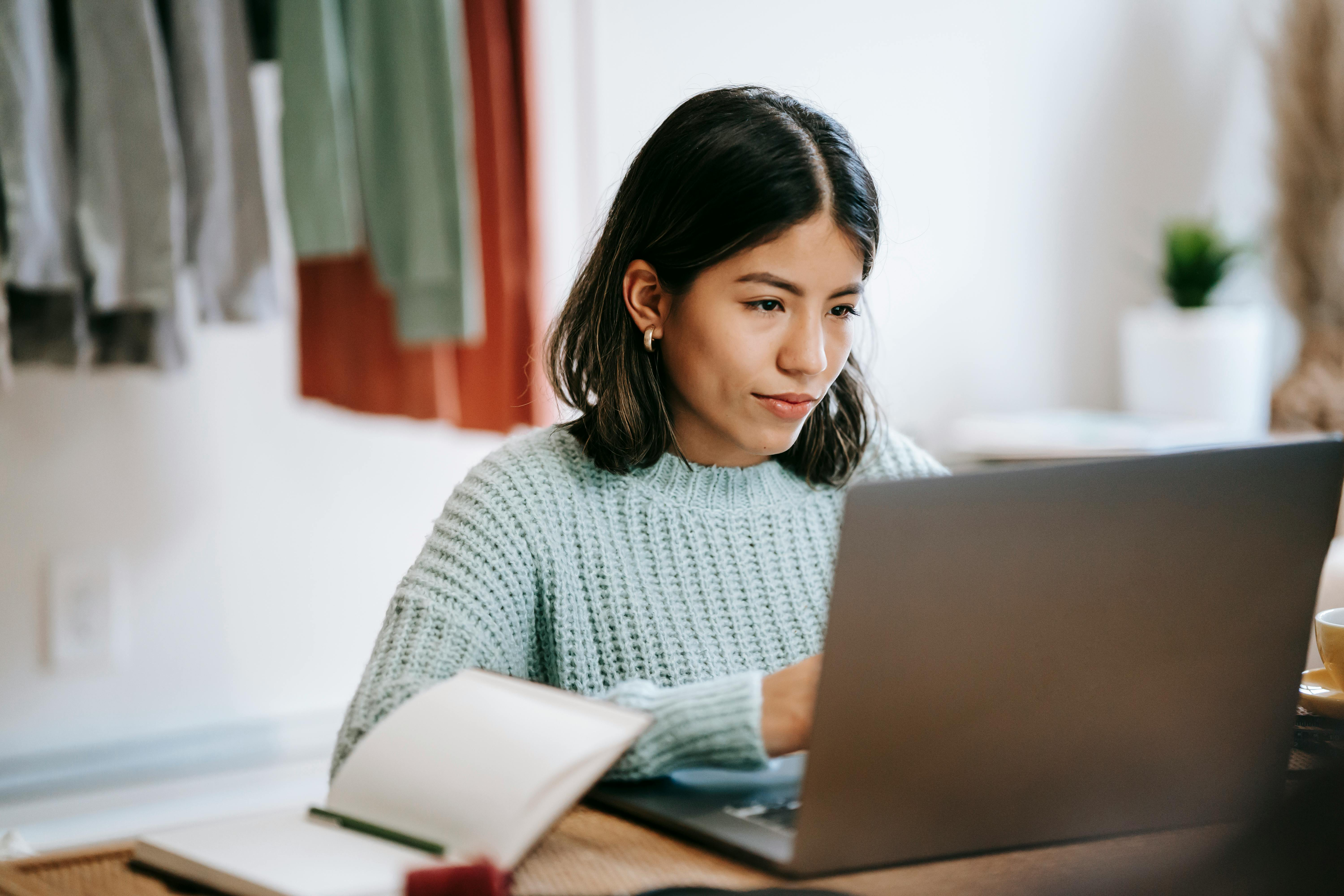 female student with black hair and a blue jumper sat in front of a laptop